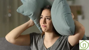 woman in grey shirt holds pillow over her ears to stop noise pollution in her home